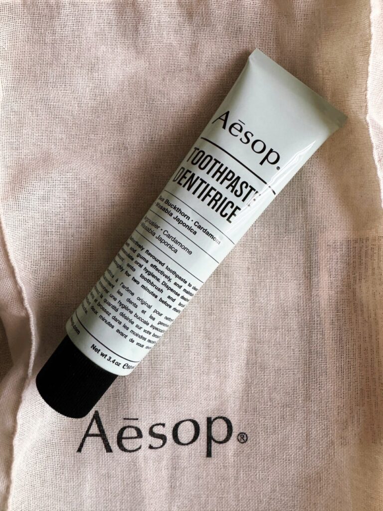 A tube of Aesop Toothpaste Dentifrice placed on an Aesop-branded fabric pouch, highlighting the minimalist packaging and product name.