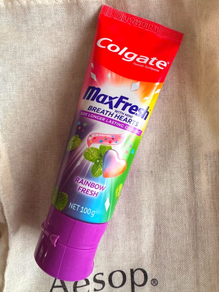 A single tube of Colgate MaxFresh Rainbow Fresh toothpaste placed on fabric, showing the colorful packaging and heart-shaped gel illustration.
