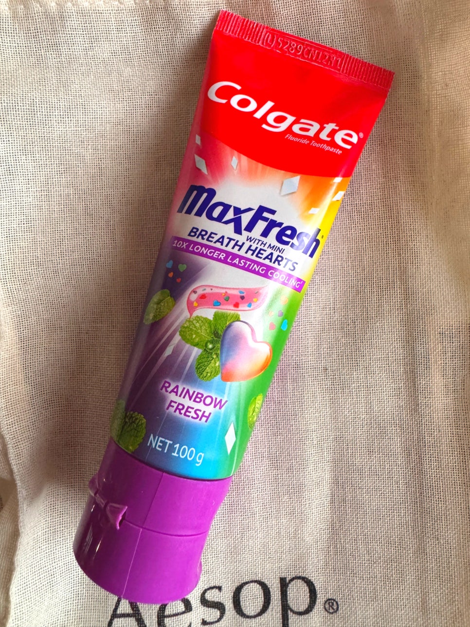 A single tube of Colgate MaxFresh Rainbow Fresh toothpaste placed on fabric, showing the colorful packaging and heart-shaped gel illustration.