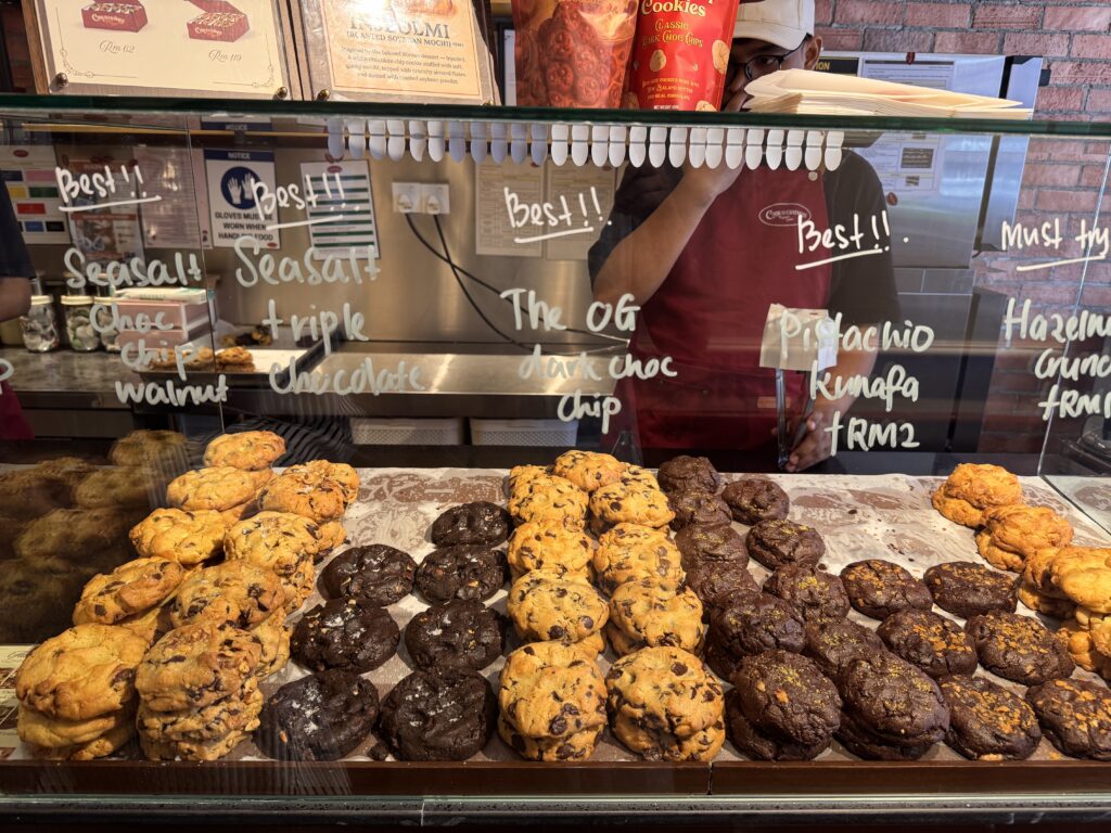 A glass display case showcasing a variety of thick, New York-style cookies and seasonal specials at Cookiecrumbs.