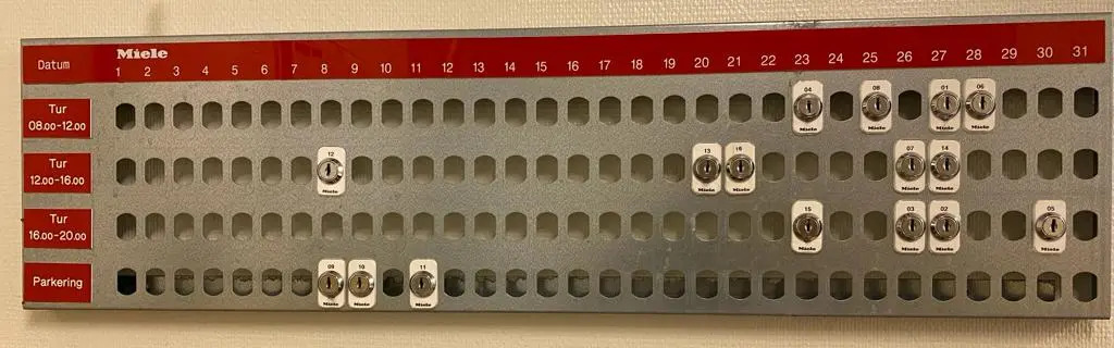 Monthly shared laundry room reservation board in a Swedish apartment building, showing booked time slots with personal key tags.