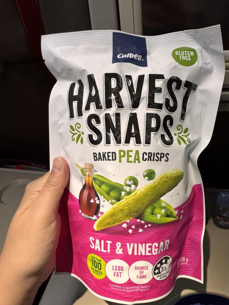 Harvest Snaps Salt & Vinegar baked pea crisps bag held in hand.