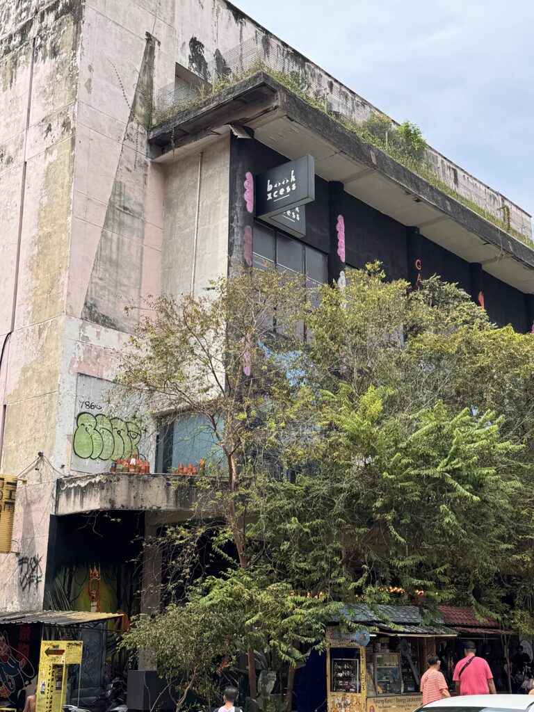 Exterior of REXKL, a redeveloped cinema building in Kuala Lumpur’s Chinatown with weathered concrete walls and greenery.