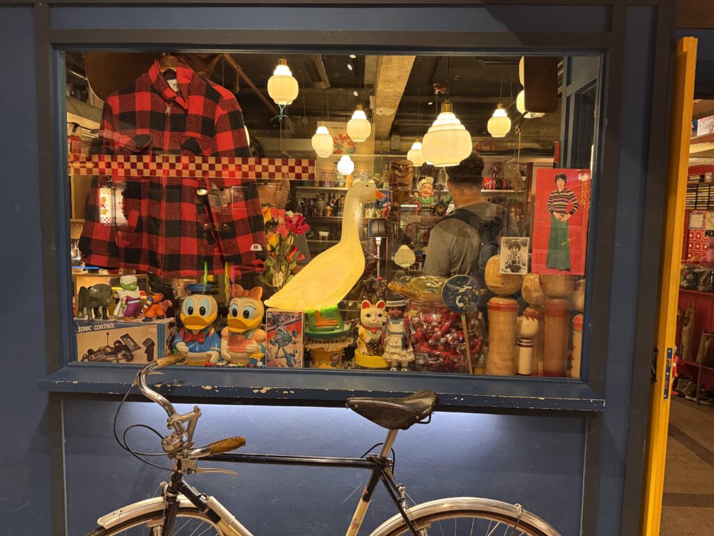 Vintage shop inside REXKL displaying retro toys, clothing, lamps, and decorative objects behind a glass window.
