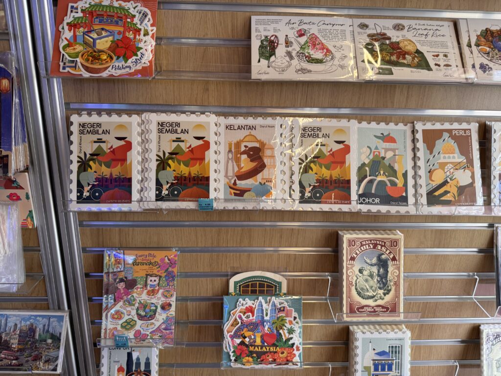 A display of illustrated paper postcards depicting Malaysian states and local food, sold at BookXcess.