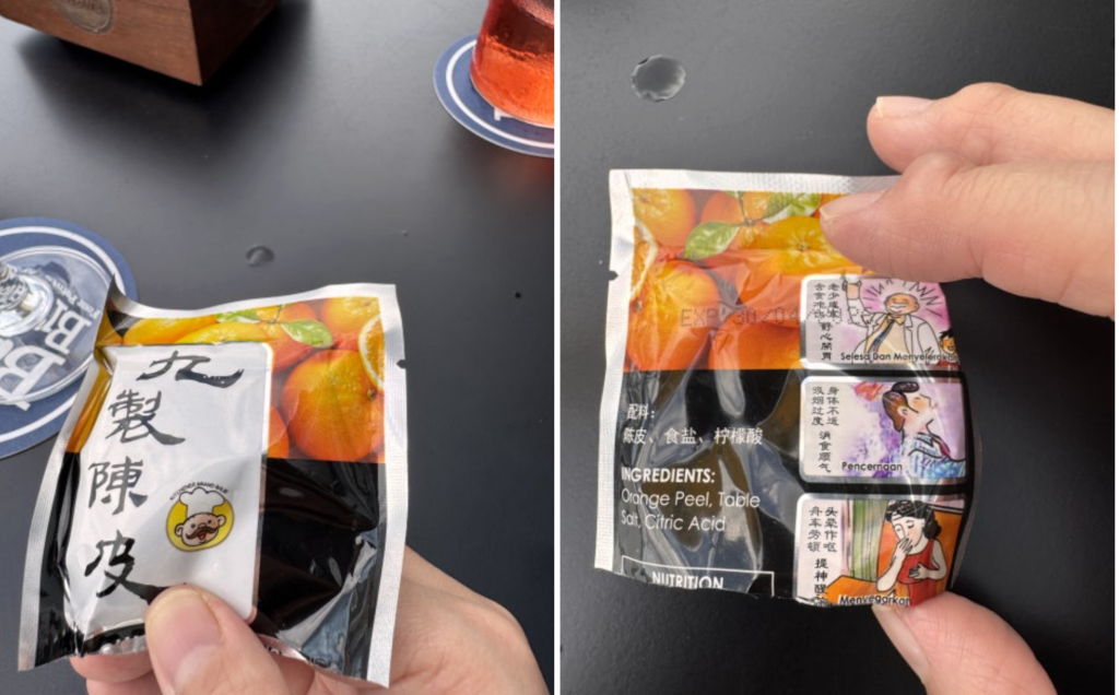 Hand holding a package of Jiuzhi Chenpi dried orange peel snack served at JANN bar KL.