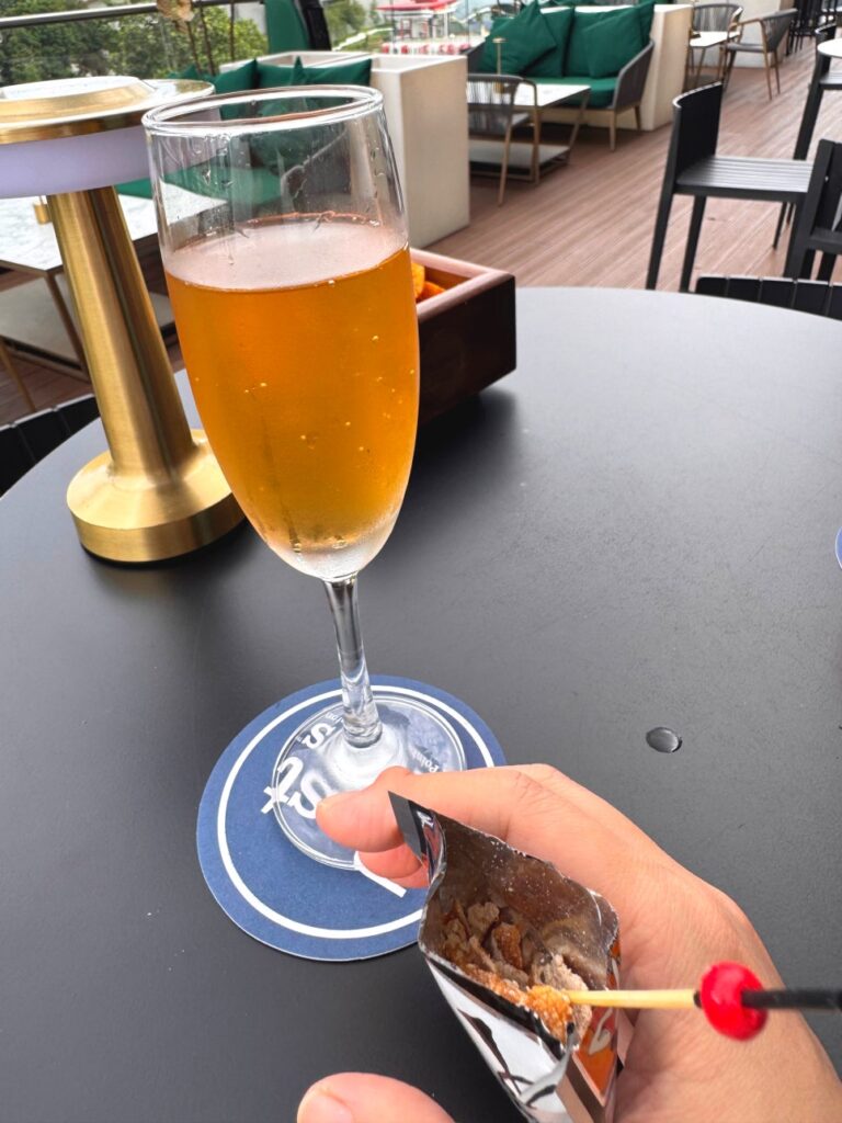 A hand holding a small silver packet of Jiuzhi Chenpi snack next to a cocktail glass.