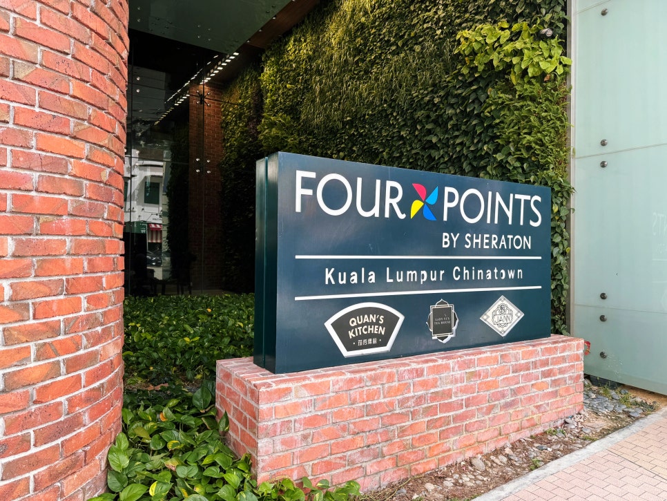 Exterior sign of Four Points by Sheraton Kuala Lumpur Chinatown surrounded by brick walls and greenery.