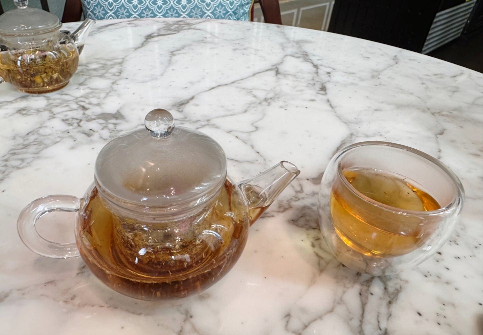 A glass teapot and teacup filled with Lady Yi’s signature blended tea on a marble table.