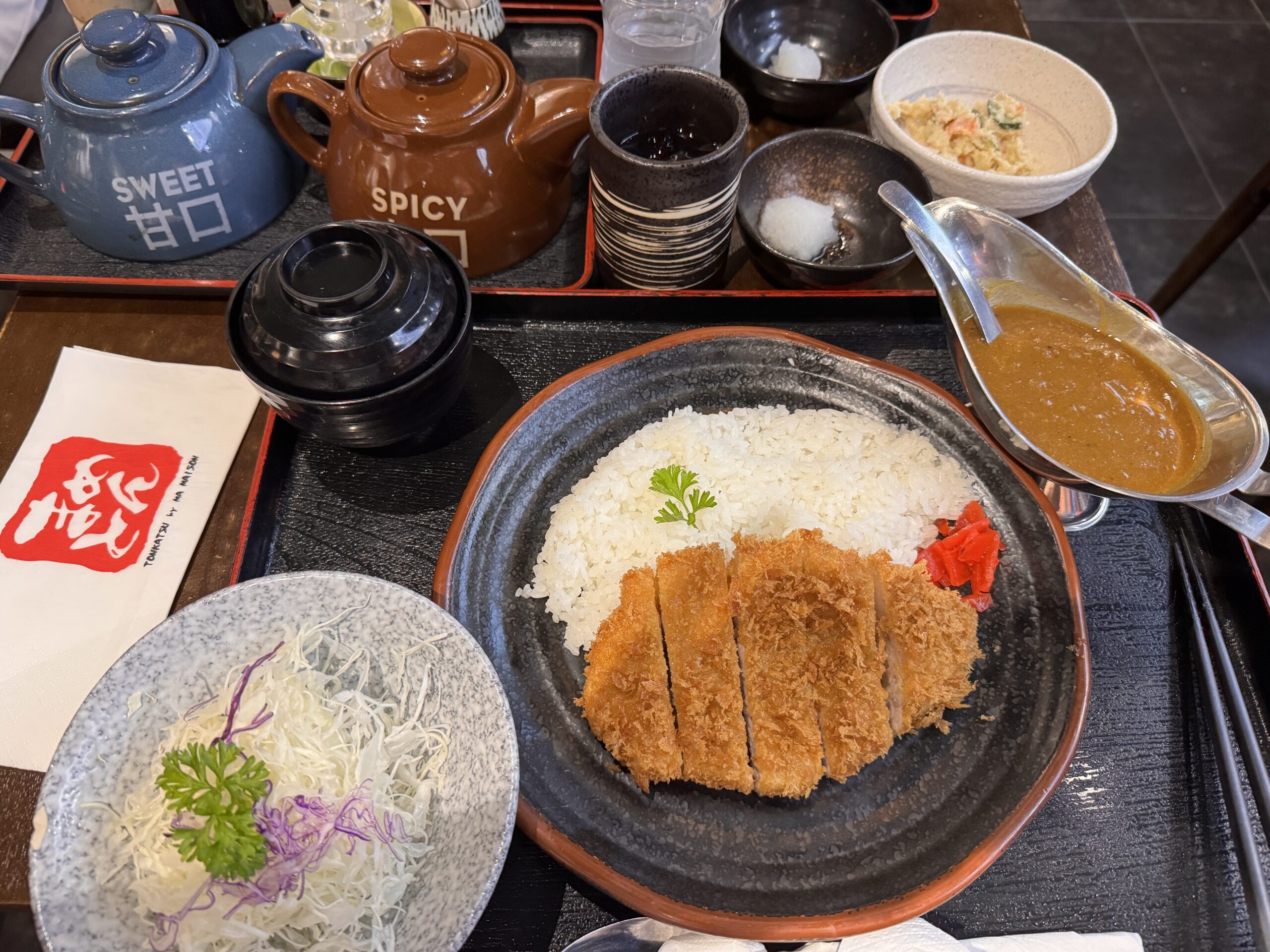 A complete Rosu Katsu Curry set at Tonkatsu by Ma Maison, including shredded cabbage, miso soup, and the signature Sweet and Spicy tonkatsu sauces.