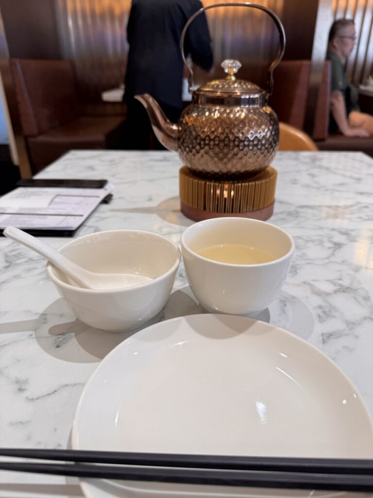 A heavy copper teapot on a candle warmer with small tea cups on a white tablecloth at Paradise Dynasty, Sunway 163 Mall.